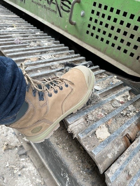 Tan work boot on a metal grate with a green machine in the background