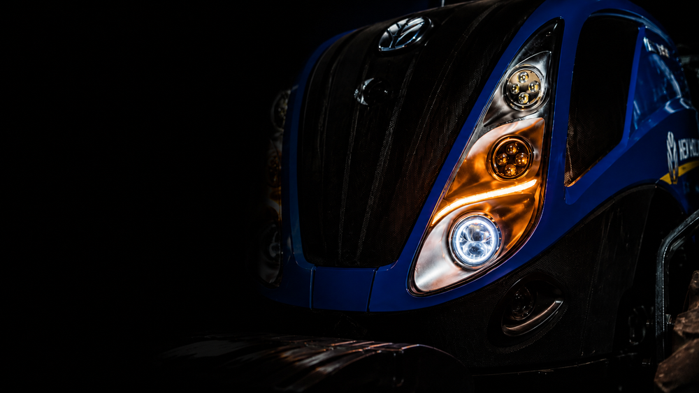 Close-up of a New Holland headlight and front grille with a dark background